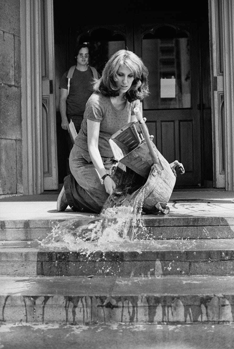 Person pouring water down steps outside a building.