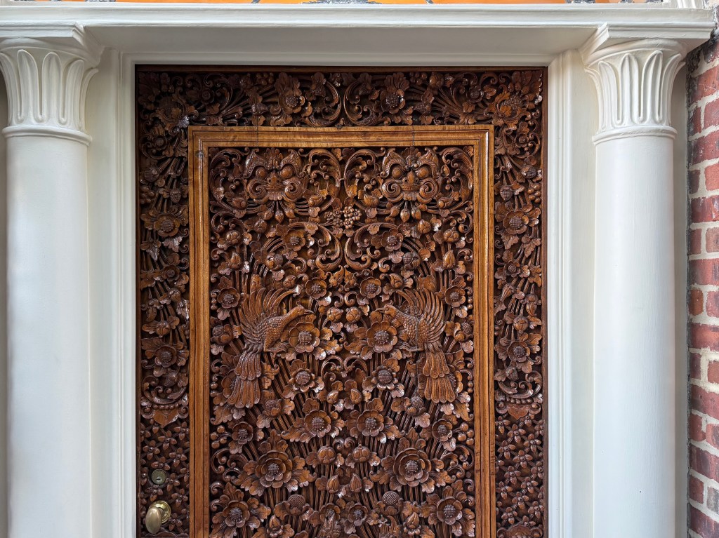 Intricate wooden door with detailed carvings of flowers and birds, framed by white columns.