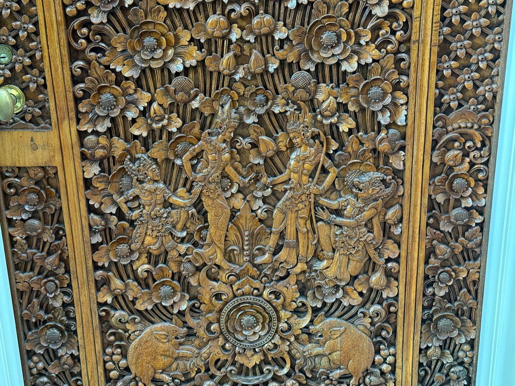 Intricate wooden carving depicting traditional figures among floral patterns, showcasing ornate craftsmanship.