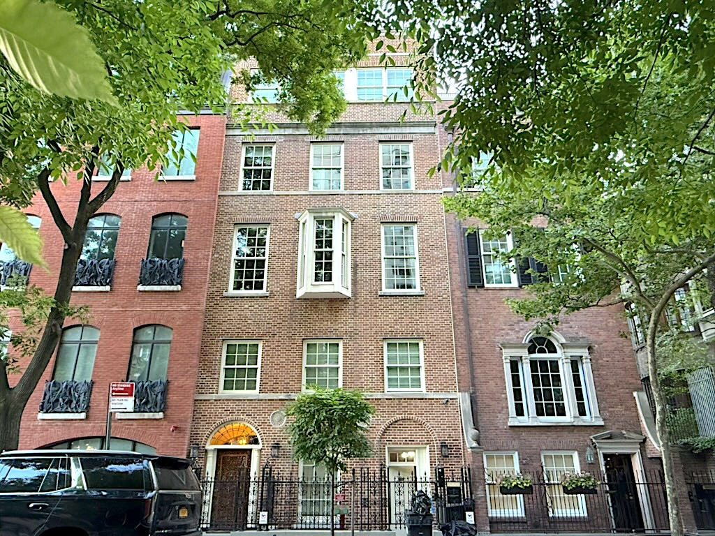 Facade of a brick building with a mix of large windows, greenery in the foreground, and a decorative entryway.