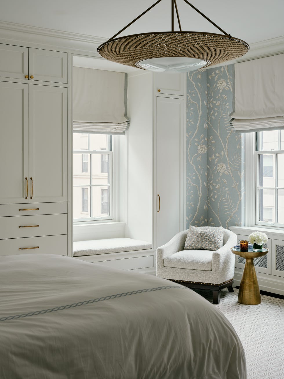 Cozy bedroom with patterned wallpaper, cushioned chair, and modern light fixture.