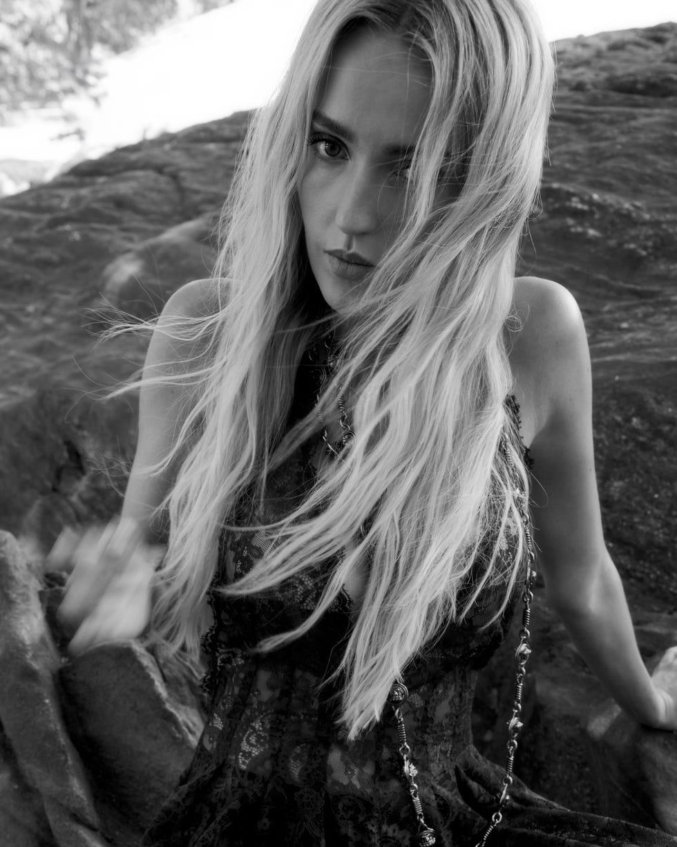 Person with long hair sitting on rocks in black and white photograph.