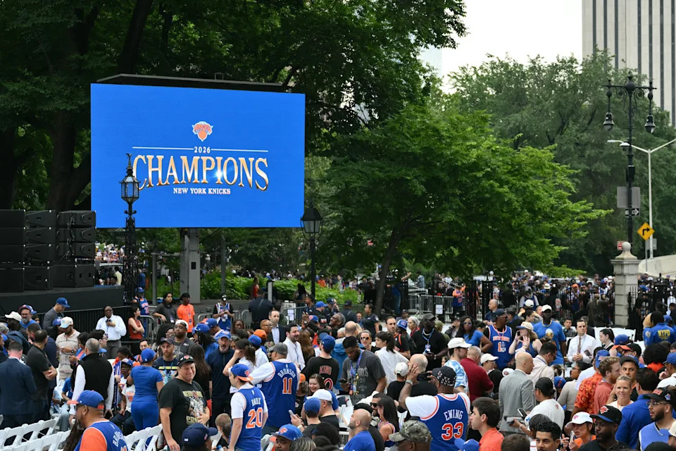 Crowd celebrating New York Knicks championship outdoors, large screen displaying "2023 CHAMPIONS" in the background