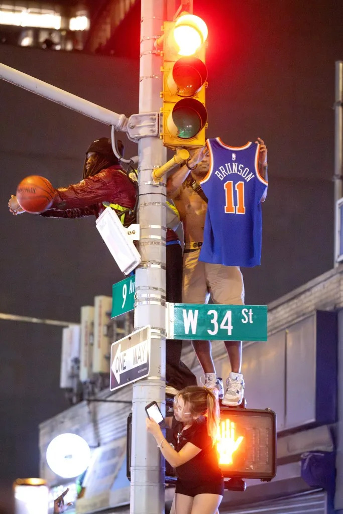 A man uses his arms as a hoop as another shows off his Knicks’ Jalen Brunson jersey on top of a pole at the intersection of W34th and 9th Avenue on June 13, 2026. Aristide Economopoulos for NY Post