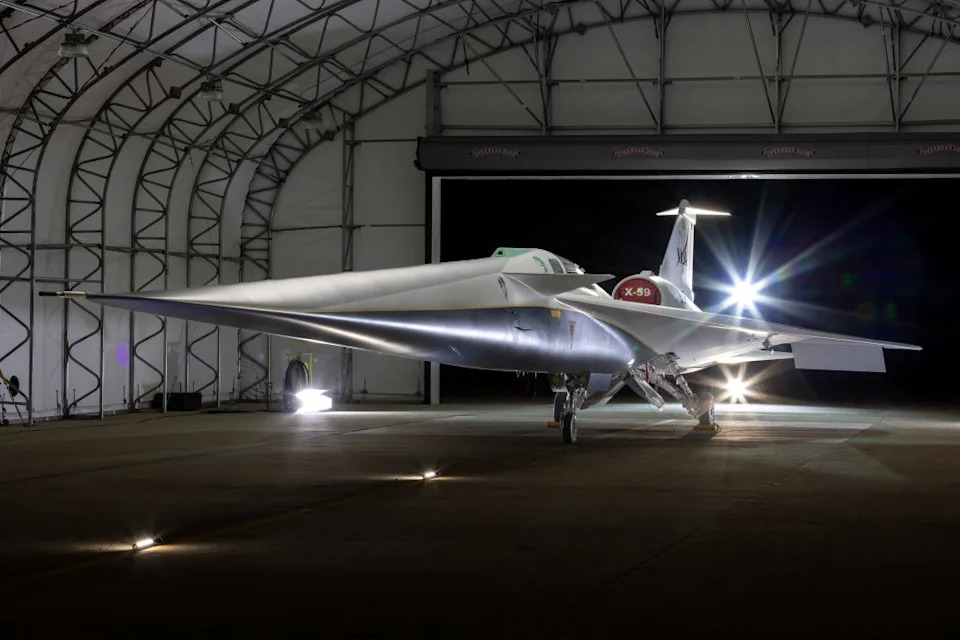 The X-59 experimental quiet supersonic aircraft in a hangar with its rear illuminated by lights. via REUTERS