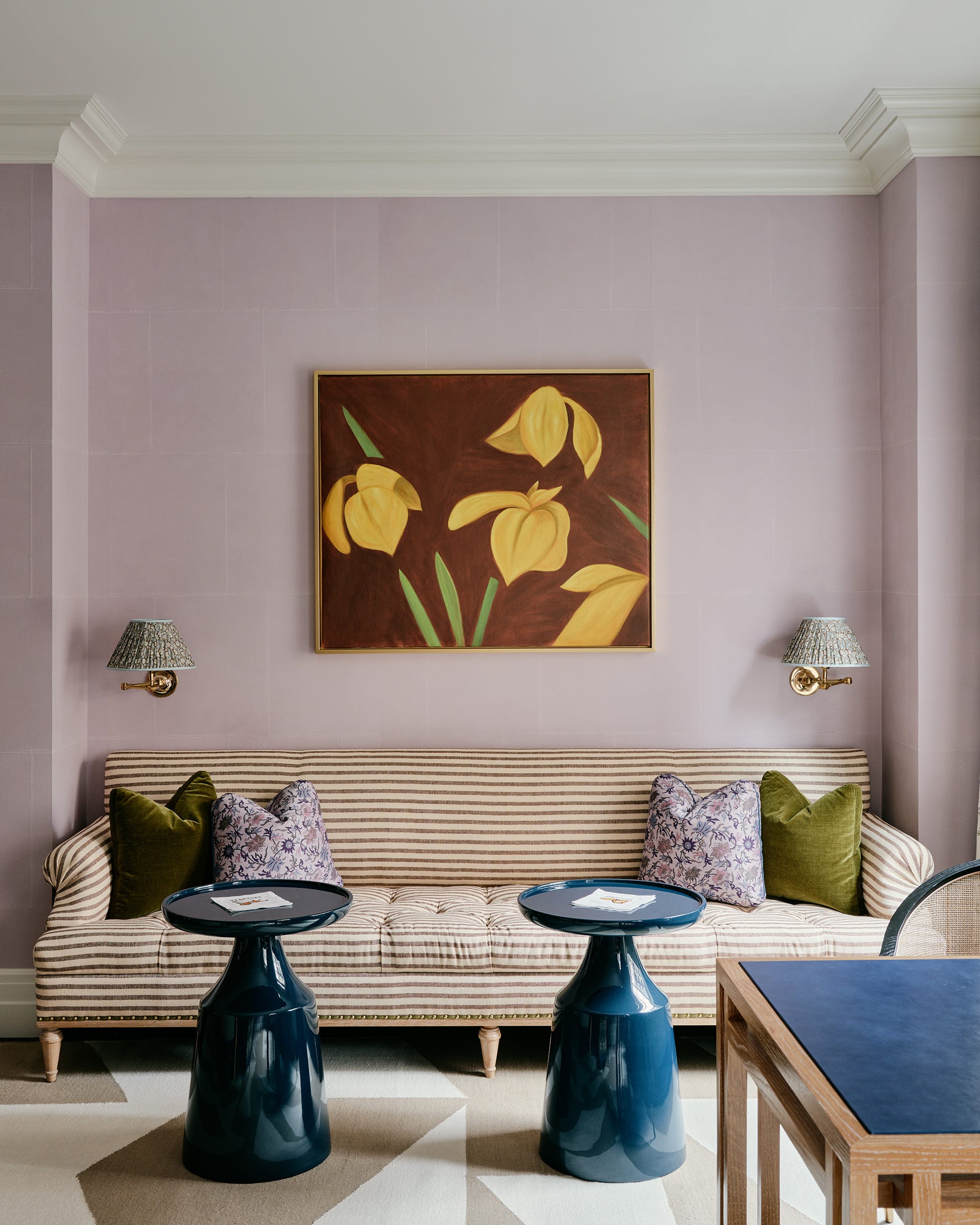 Living room with striped sofa, yellow flower painting, and round mirror above fireplace