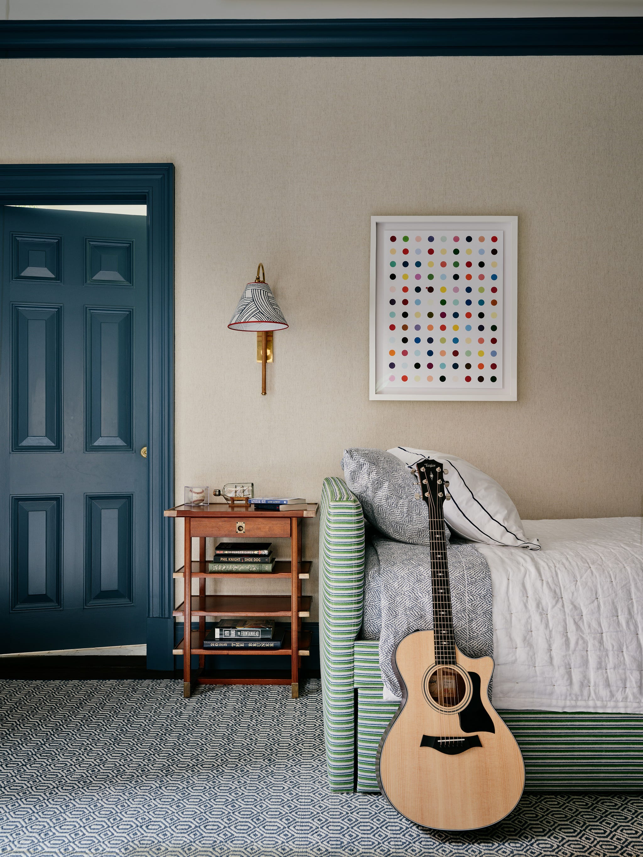 Cozy bedroom with a guitar leaning against a bed, colorful polka dot artwork, and a blue door.