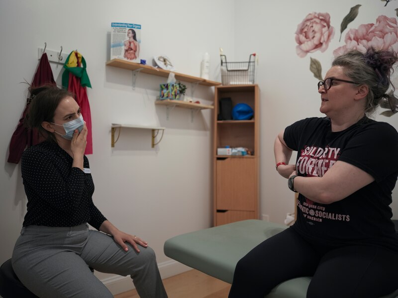 A photograph of a physical therapist sitting on the left, listening to her patient on the right as she describes her condition.