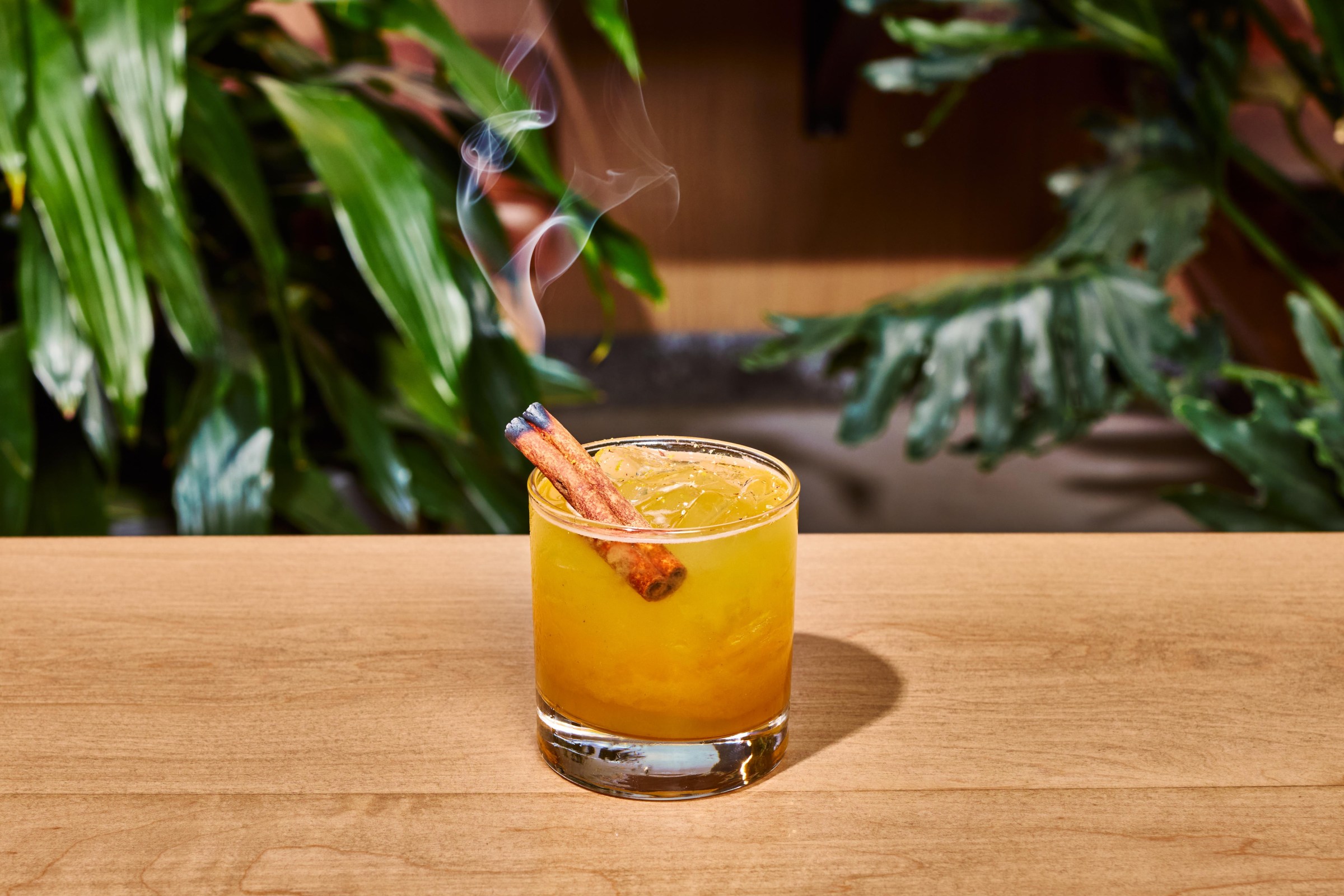 A pale orange cocktail with a cinnamon stick in it.