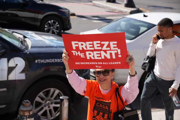 A member of Community Action for Safe Apartments (CASA) holds a "Freeze the Rent" sign while marching down Grand Concourse.