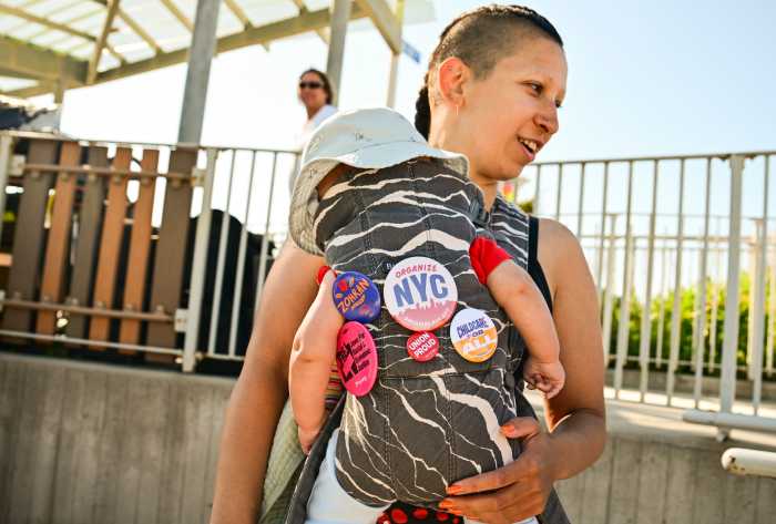 A Organizer carries a baby with pins supporting Mayor Zohran Mamdani and 2-K for all ahead of a press conference on Tuesday, June 2nd at Beach 108 Street and Shore Front Parkway in Rockaway Park.