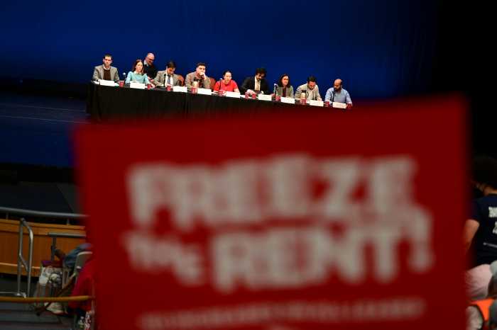 rent guidelines board meets in background as someone holds up sign demanding a rent freeze
