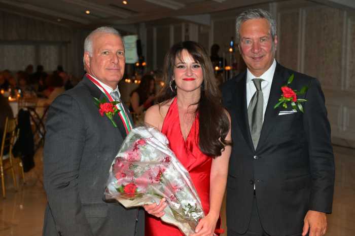 woman in red dress holding flowers with two men in suits at her side