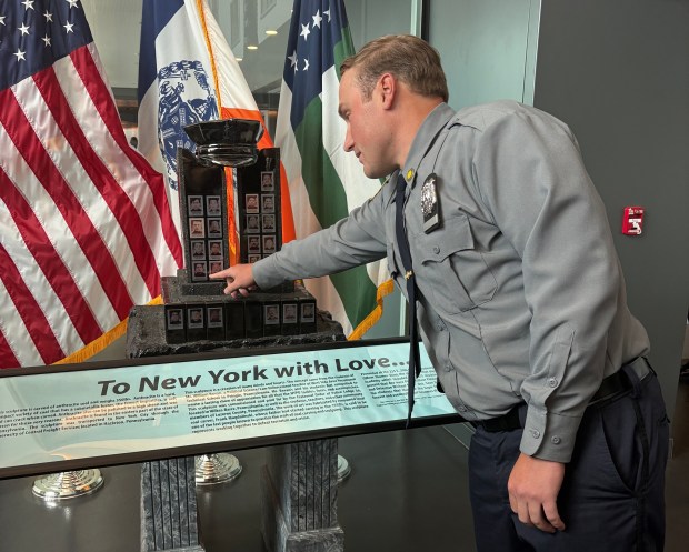 NYPD graduate Casey Kloepfer points to his father's picture on a 9/11 memorial on Tuesday, June 23, 2026, in Queens, New York. (Roni Jacobson / New York Daily News)
