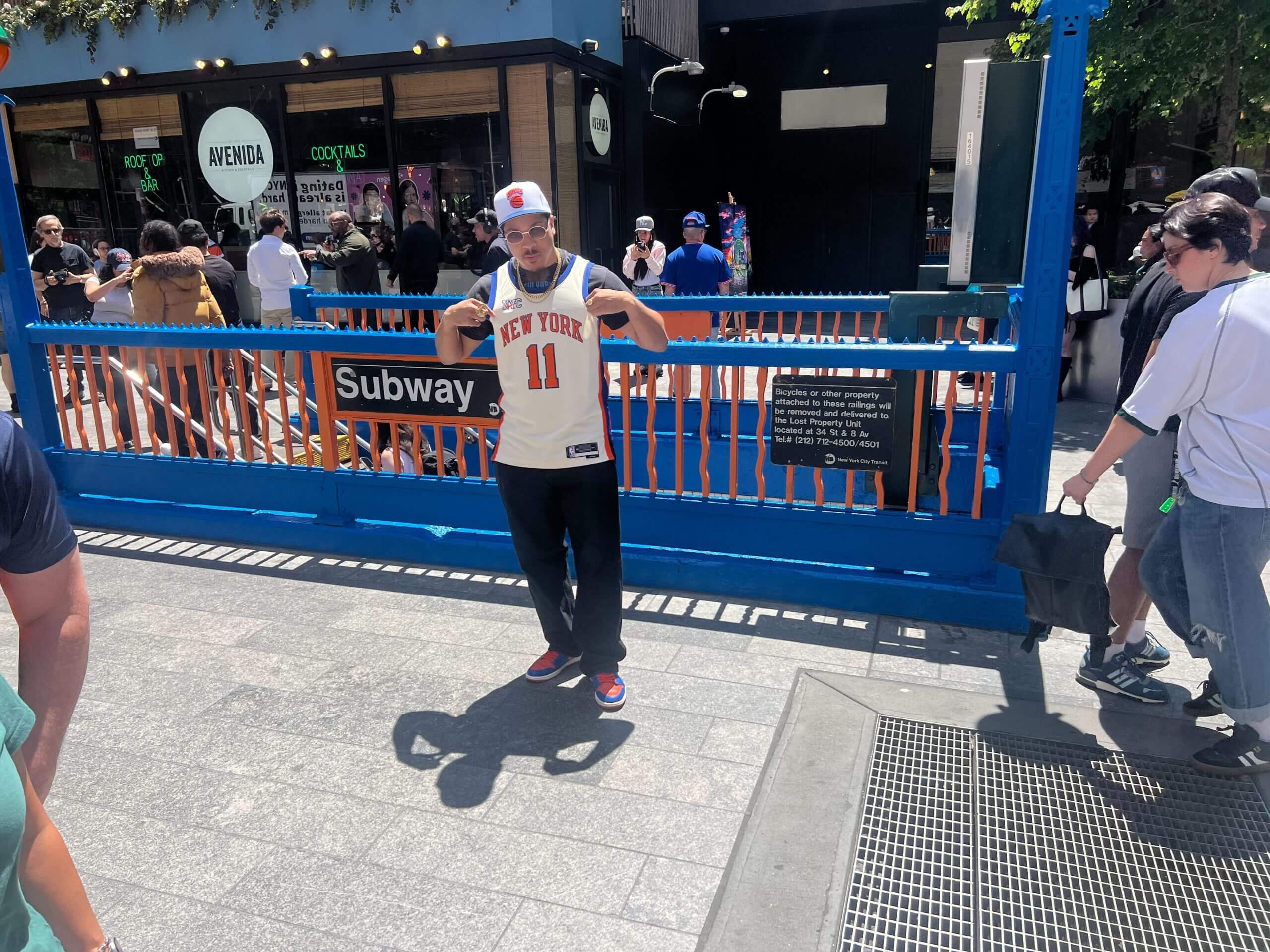 A Knicks fan poses in front of the blue-and-orange subway entrance near Madison Square Garden.