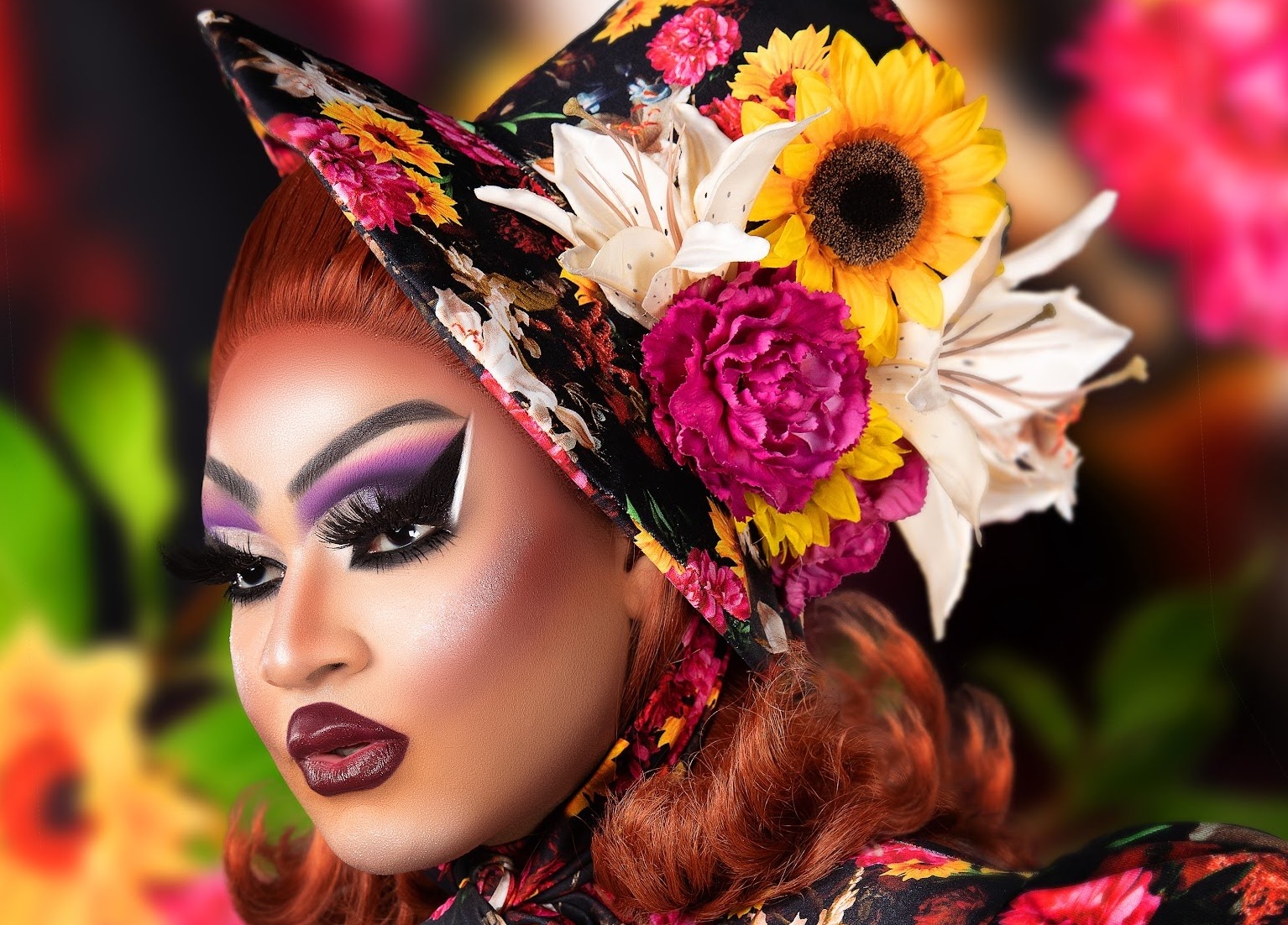 close-up side profile photo of a drag queen in heavy makeup wearing a hat decorated with artificial flowers