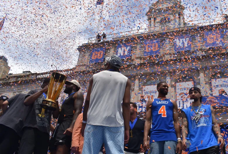 New York Knicks pose with their 2026 trophies as confetti rains down at their City Hall celebration. (Ariama C. Long photo)