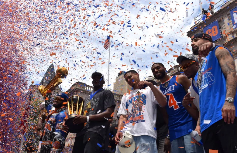 New York Knicks pose with their 2026 trophies as confetti rains down at their City Hall celebration. (Ariama C. Long photo)