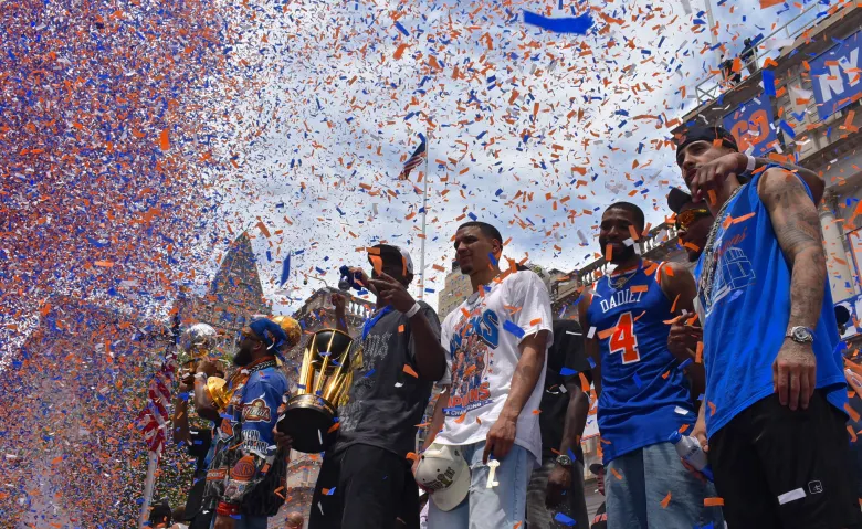 New York Knicks pose with their 2026 trophies as confetti rains down at their City Hall celebration. (Ariama C. Long photo)