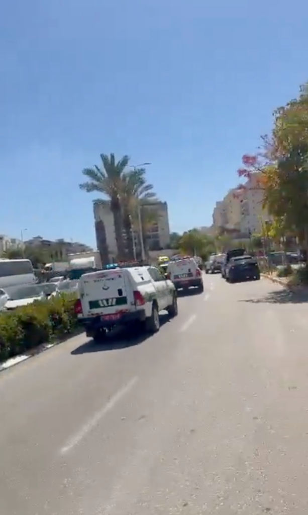 White Magen David Adom vehicles on a sunny street with palm trees and buildings.