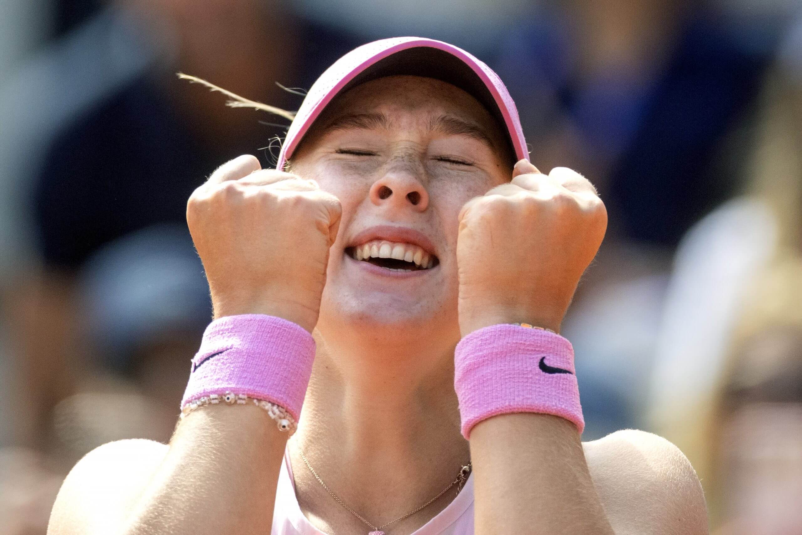 Mirra Andreeva clenches her fists in celebration with her eyes closed wearing two pink wristbands.