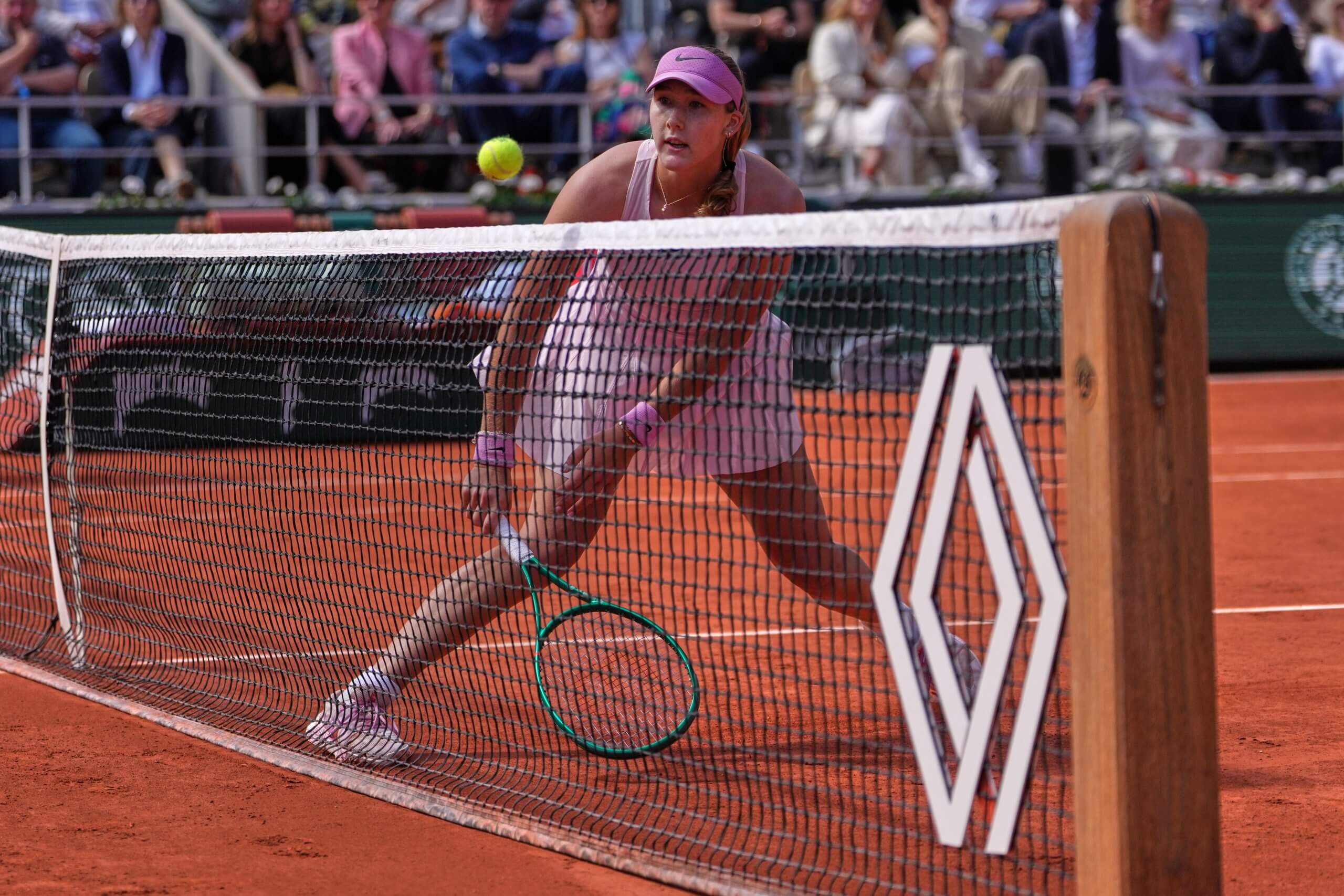 Mirra Andreeva watches a tennis ball as it hangs over the net on a clay court.