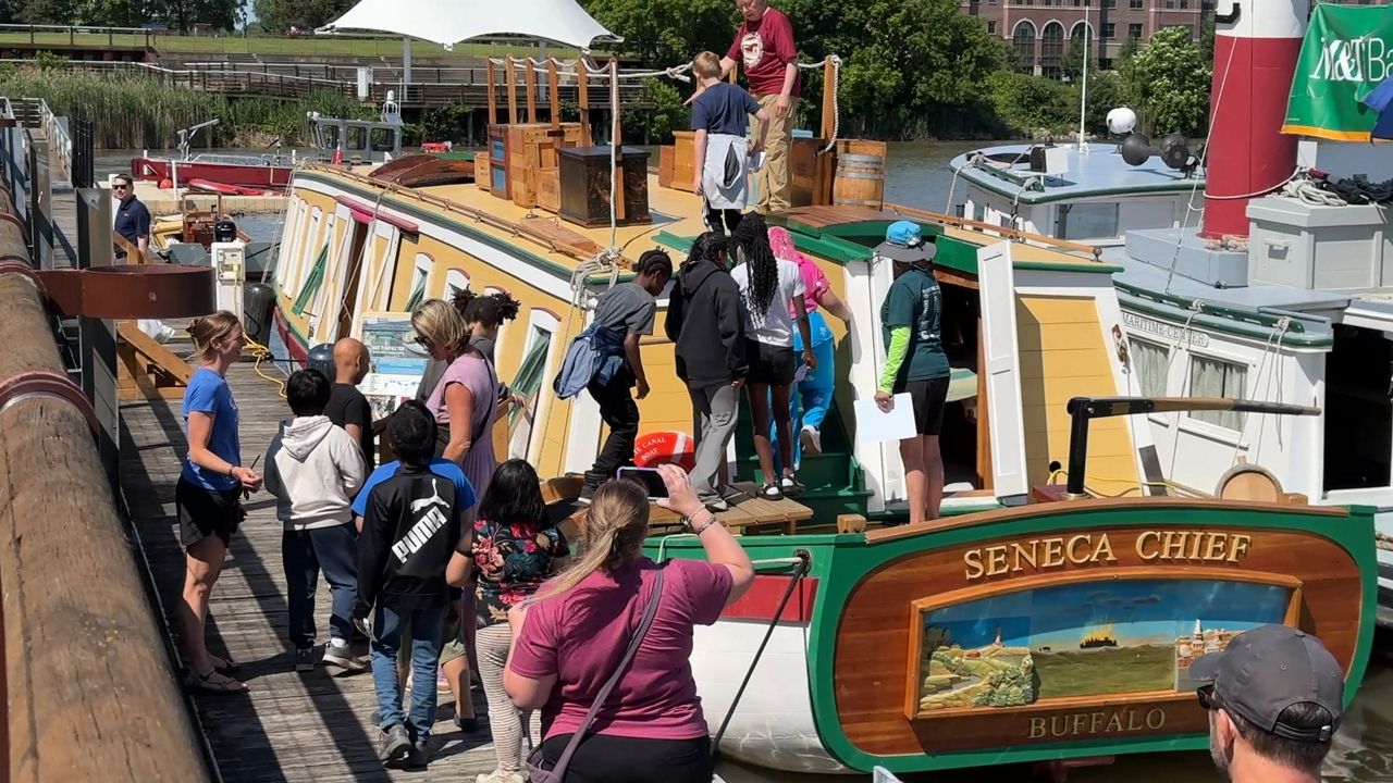 photo of a line of children and adults standing next to and walking onto a boat which reads seneca chief buffalo