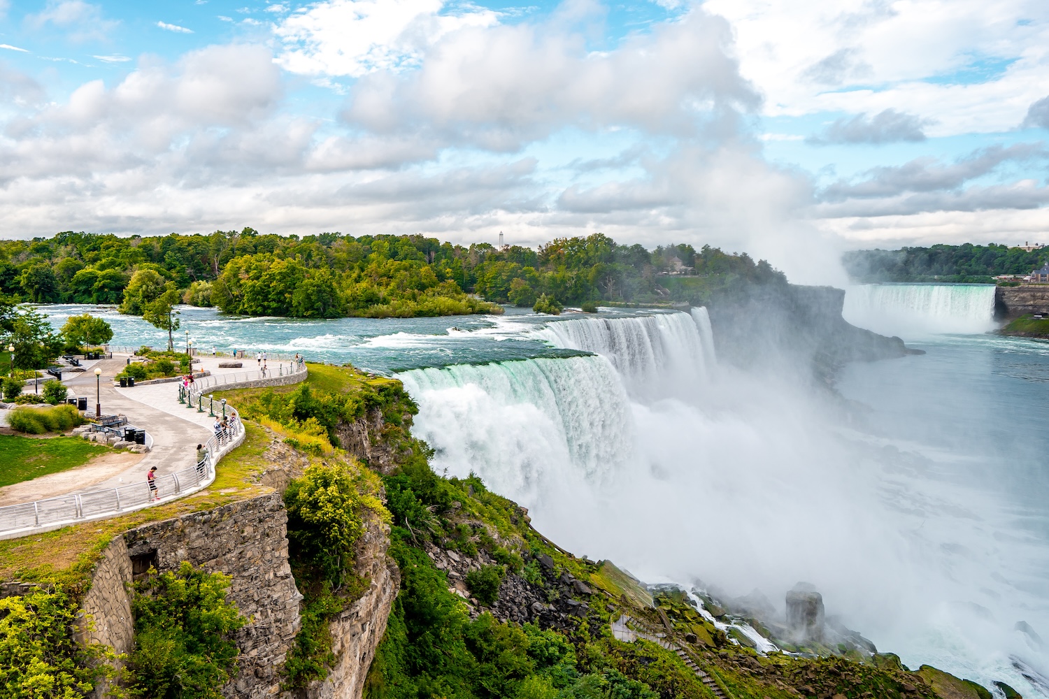 View of Niagara Falls with mist rising above the gorge and observation paths nearby.