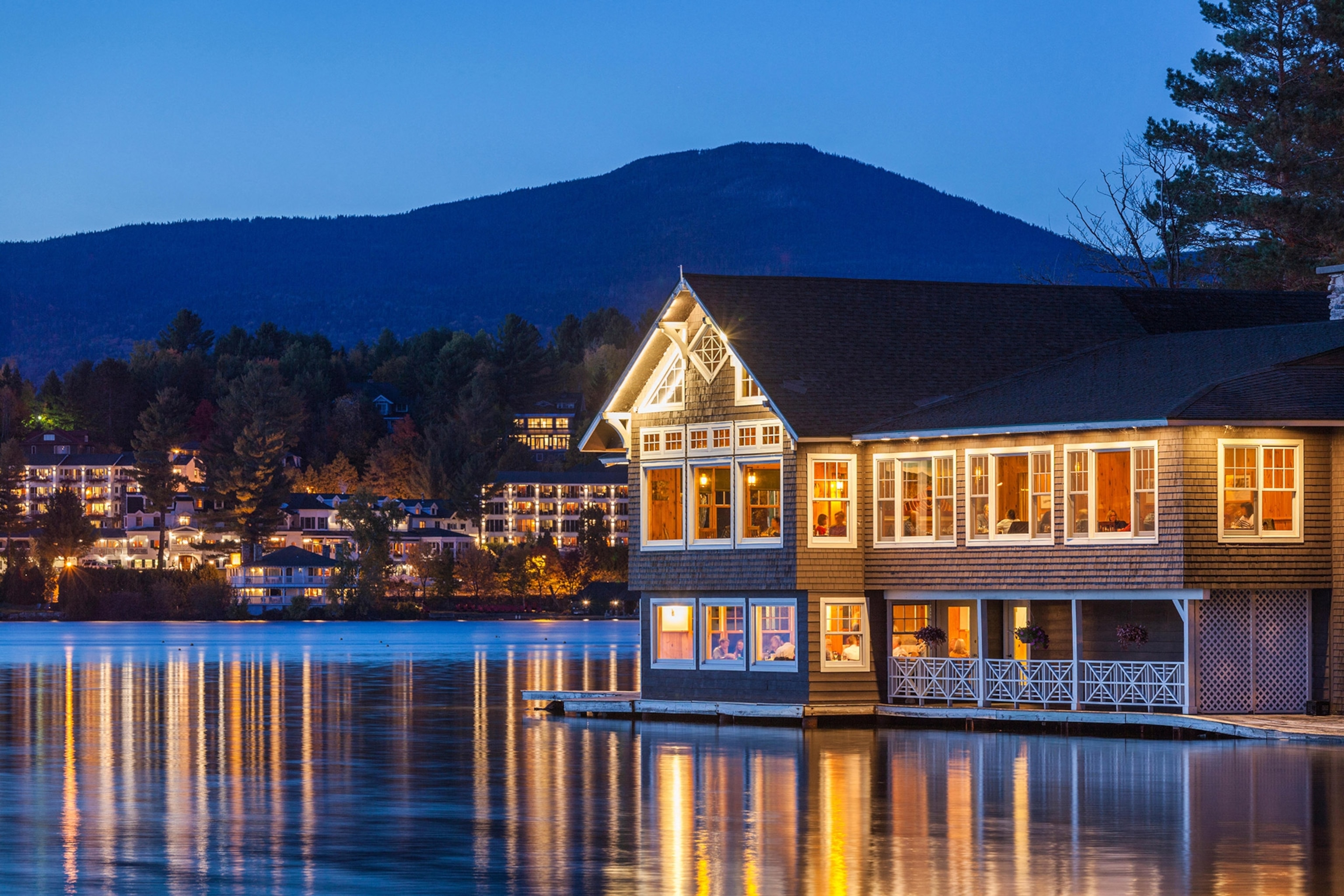 A nighttime view of a lakeside restaurant aglow with lights, reflected in water