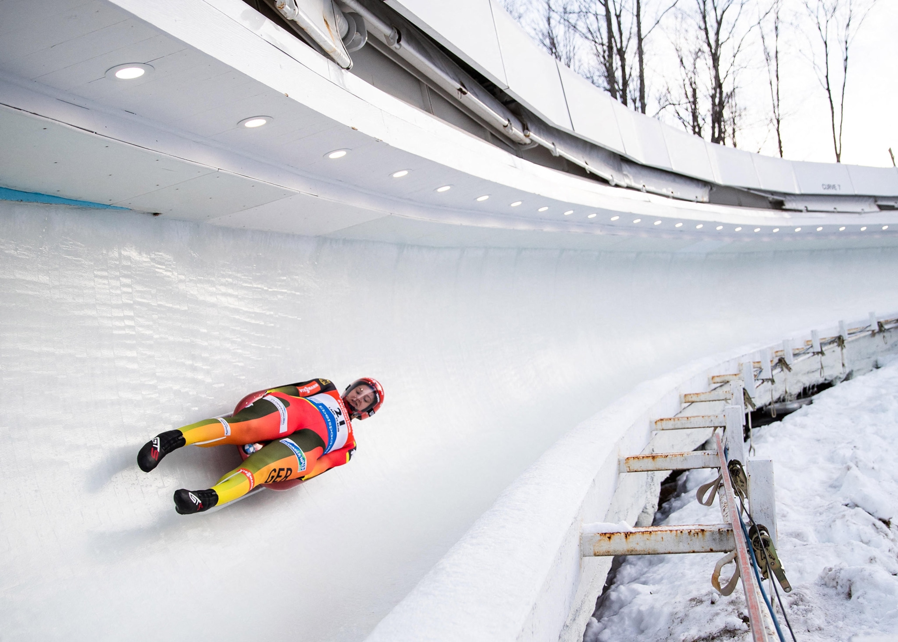 A person in aerodynamic suit slides feet-first and on their back along an ice track