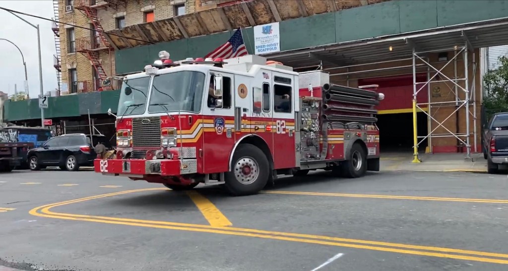 A red and white FDNY fire truck with unit number 82 driving out of a fire station.