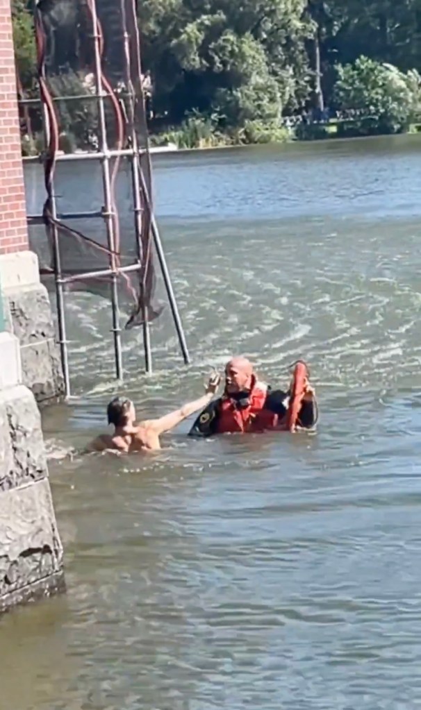 A person in a life vest extending their hand to a person in the water near a brick structure.