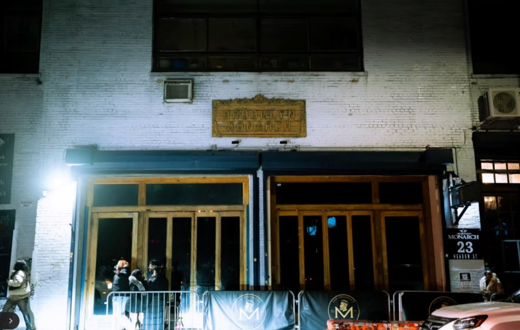 The exterior of Brooklyn Monarch music venue at night, with people waiting in front of its wooden doors.