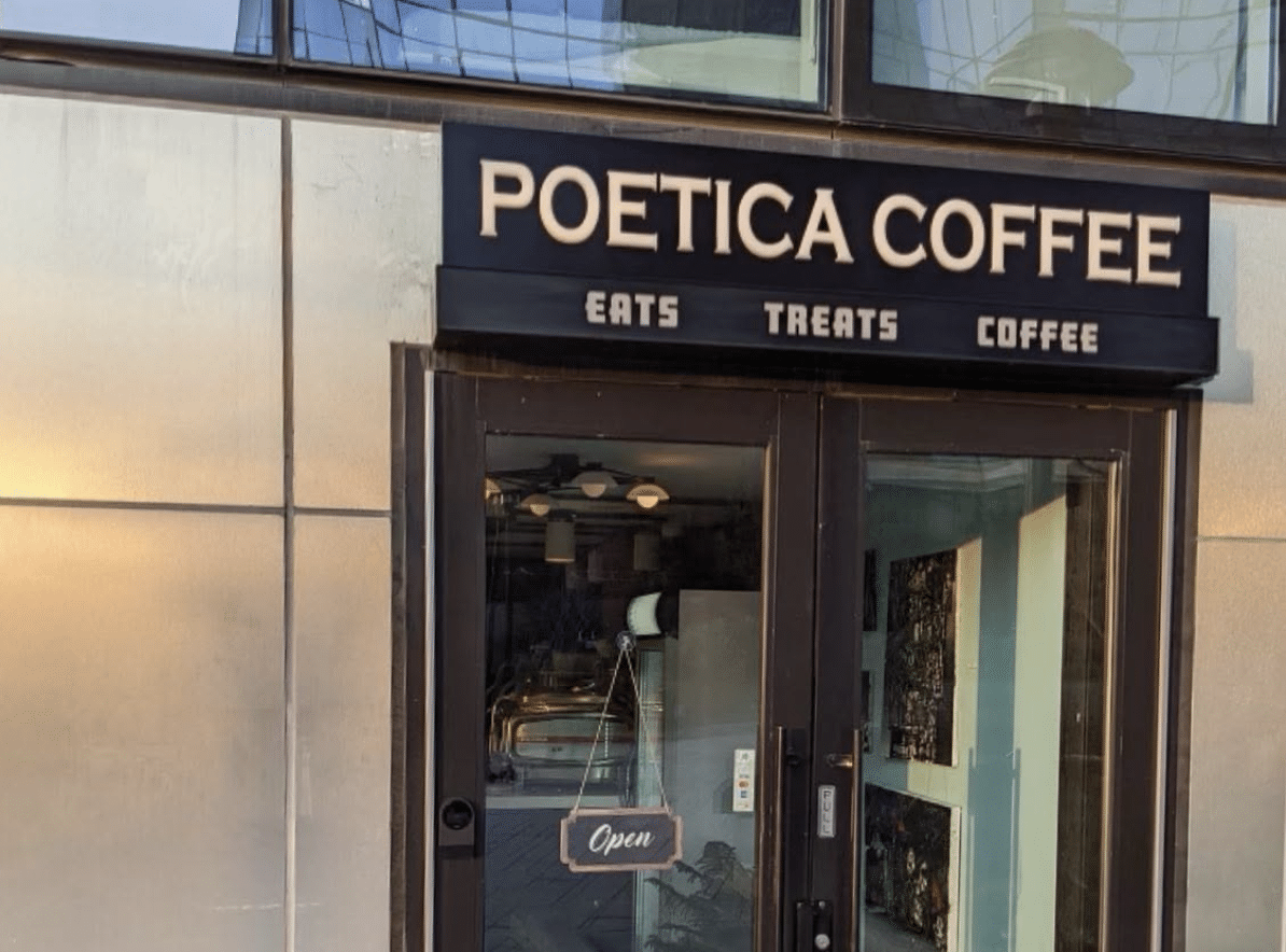Entrance to a Poetica Coffee location in New York City, featuring the café's black storefront sign above glass doors and windows.