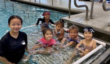 children smile while taking part in a swimming lesson at an indoor pool