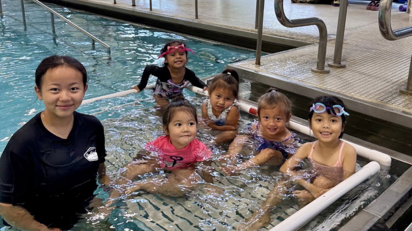 children smile while taking part in a swimming lesson at an indoor pool