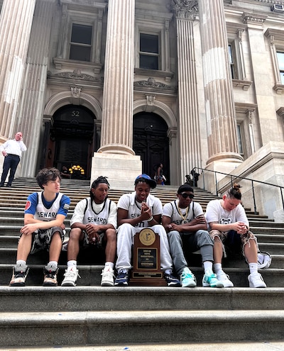 Five male students sit on the steps o a building with columns.