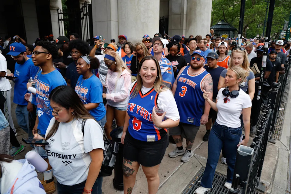 A crowd of fans wearing New York basketball jerseys and casual wear gather excitedly outside a venue