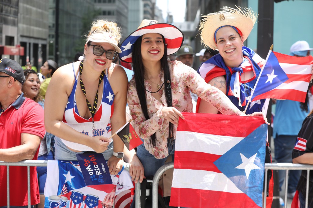 Three women holding Puerto Rican flags and smiling at the annual Puerto Rican Day Parade.
