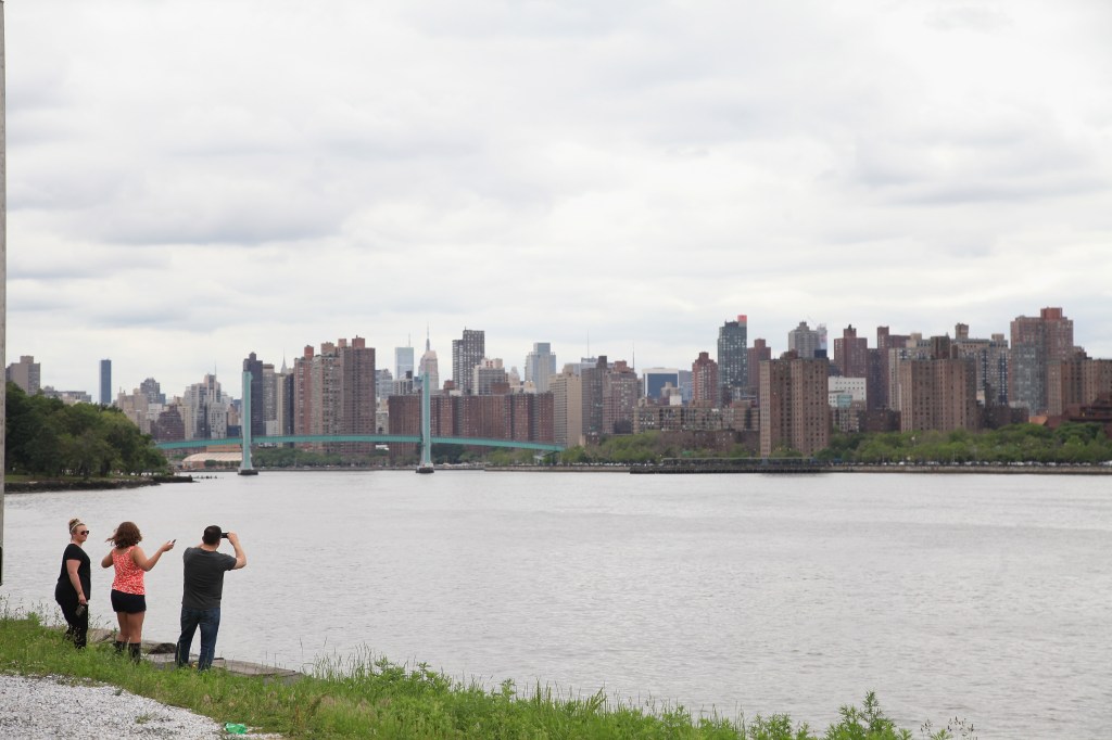 Three people standing by the water, looking at the city skyline with a bridge in the distance.