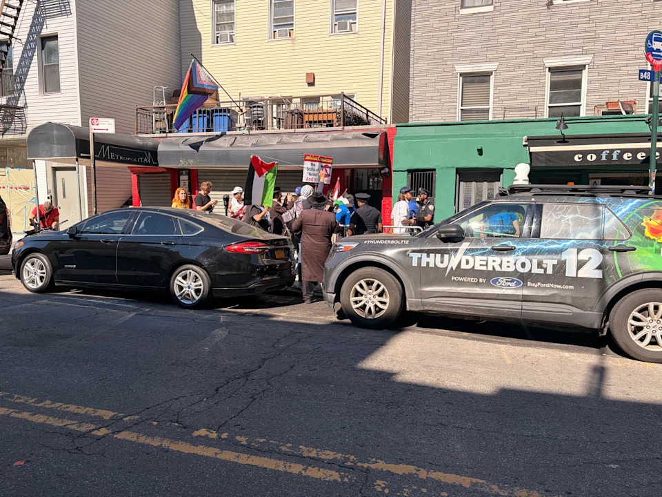 A small group of protestors hold a Palestinian flag and an anti-Israel sign outside a coffee shop.