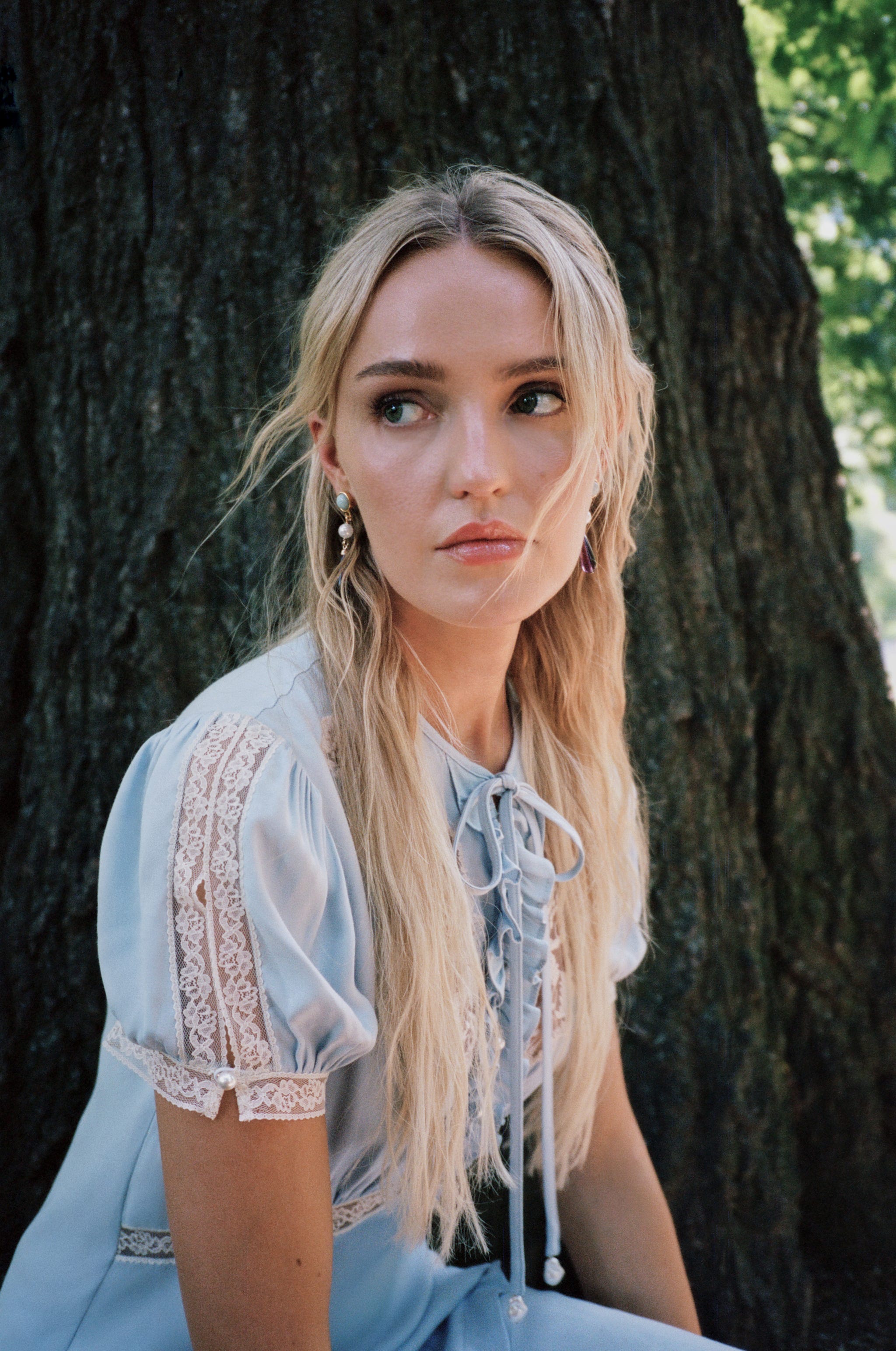 Woman with long blonde hair in blue dress sitting by tree