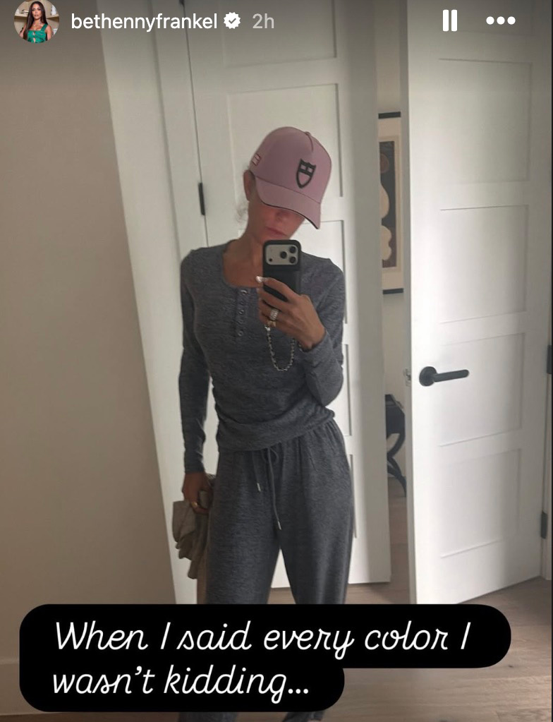 Bethenny Frankel taking a mirror selfie wearing a matching gray loungewear set and a pink baseball cap.