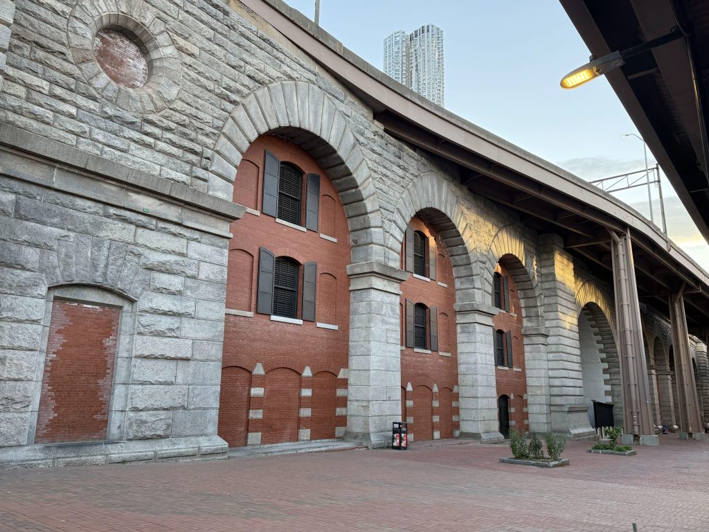 Historical brick and stone archway structure with windows, situated alongside a paved walkway.