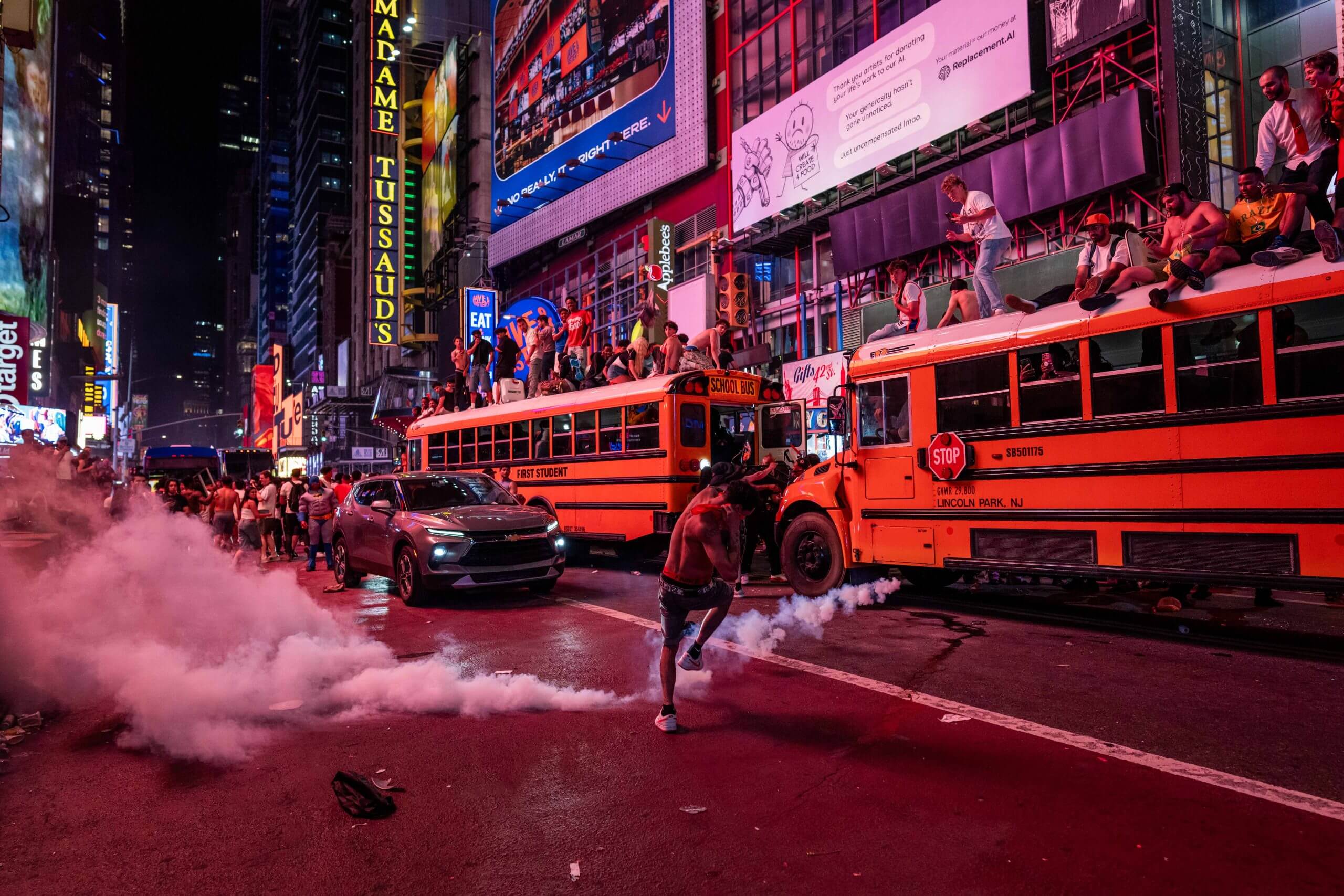 People sitting on top of yellow buses as a man kicks a smoke bomb