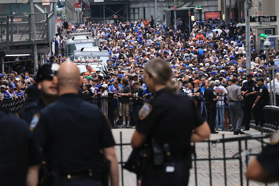 Large crowd gathered in city street, with police officers in foreground monitoring the scene