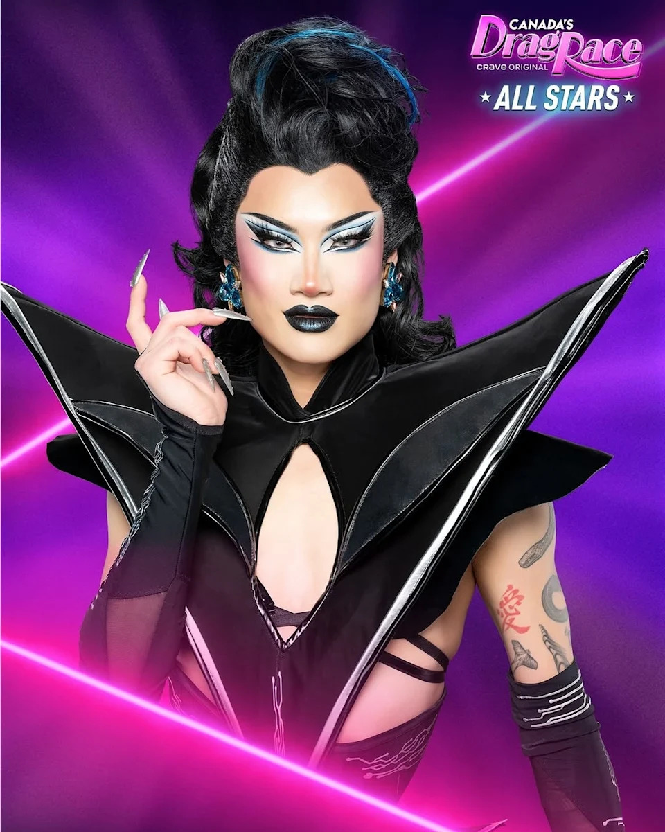 Drag performer in a futuristic, angular black outfit with bold makeup and styled hair, posing against a "Canada's Drag Race: All Stars" backdrop