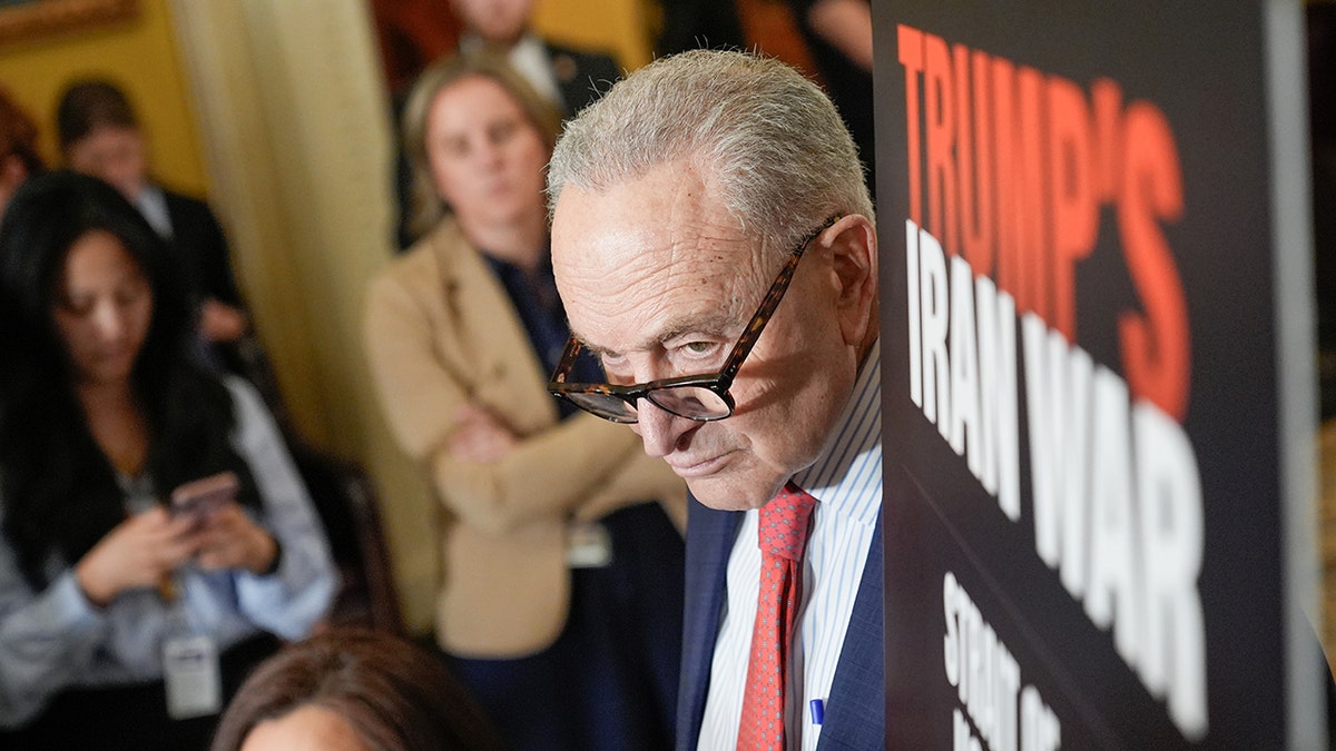 Chuck Schumer listening while standing at a podium during a news conference.