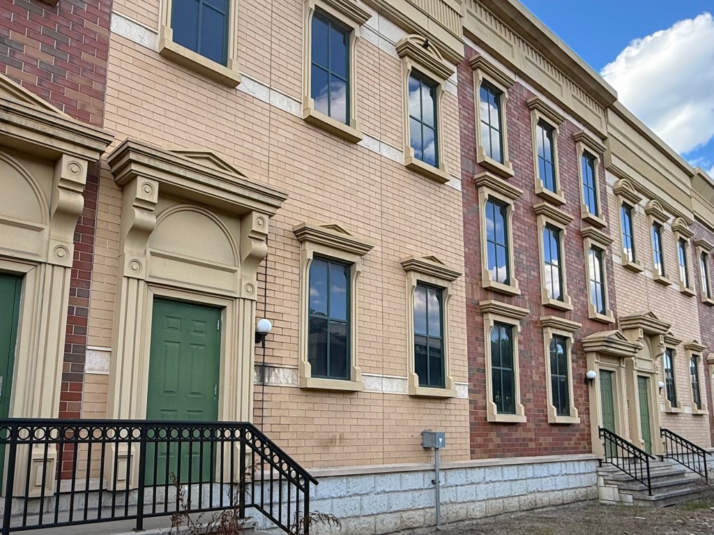Exterior view of a multi-story building featuring a combination of beige and red brick, decorative architectural elements, and green doors.