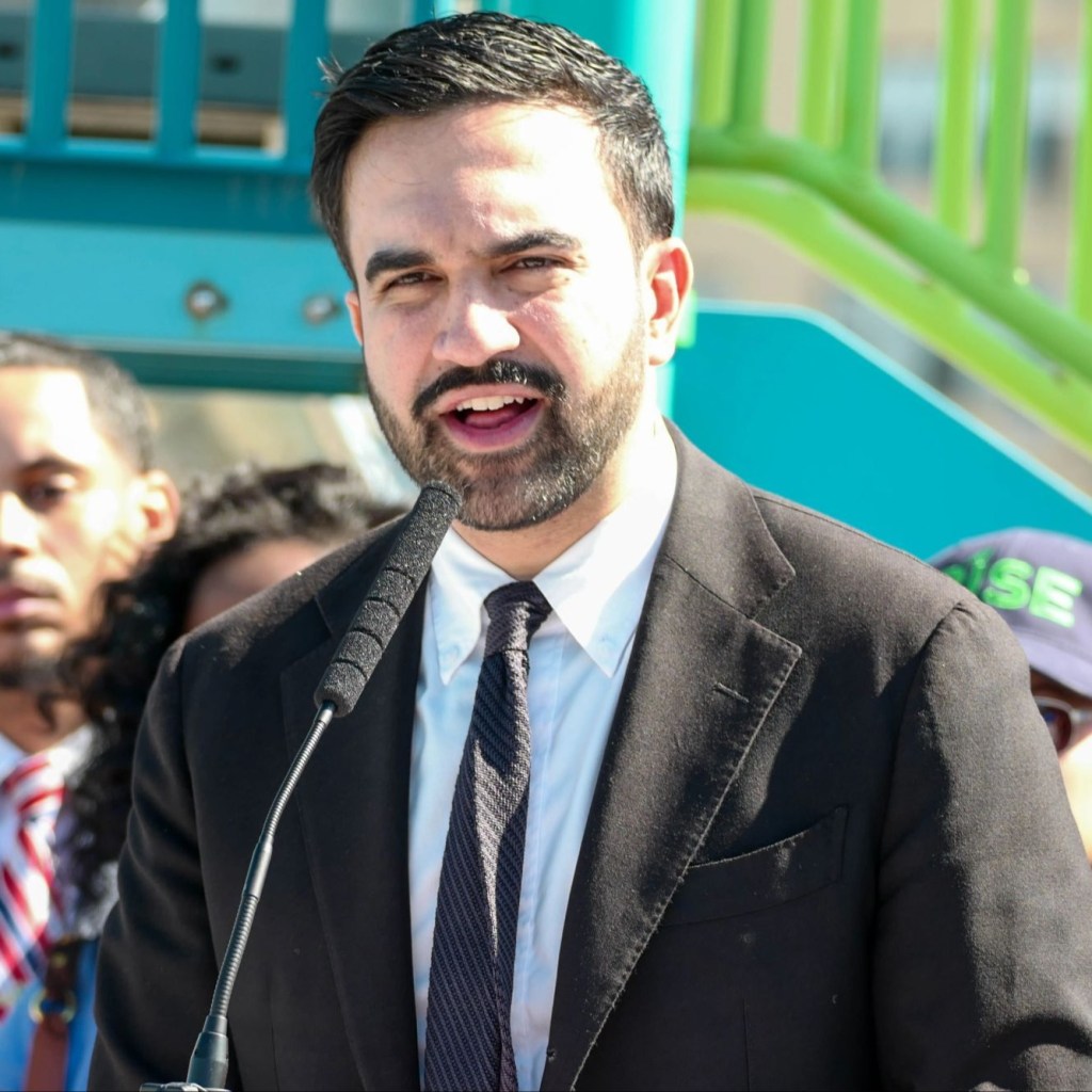 Mayor Zohran Mamdani speaks at a podium with a sign reading "CHILD CARE for ALL" and "2-K APPLICATIONS ARE OPEN."